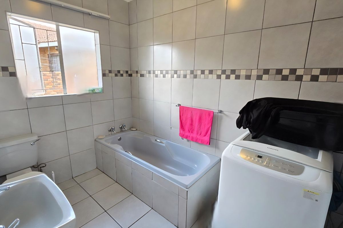 A functional bathroom featuring a built-in bathtub, toilet, and washbasin, finished with neutral ceramic wall and floor tiles.