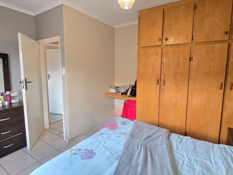 A bedroom featuring built-in wooden cupboards, a built-in desk, and tiled flooring, offering functional storage and a neutral layout.