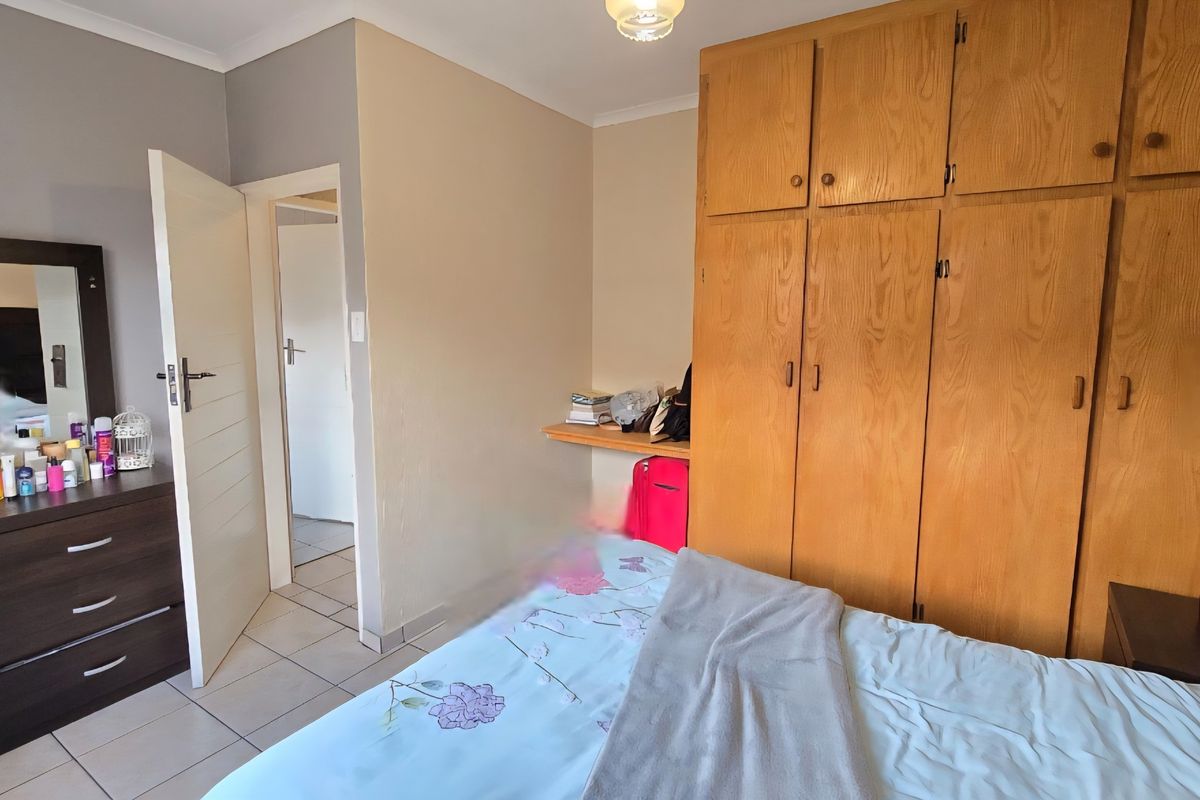 A bedroom featuring built-in wooden cupboards, a built-in desk, and tiled flooring, offering functional storage and a neutral layout.