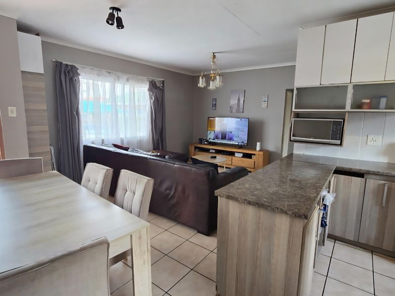 Open-plan living and dining area featuring a functional kitchen with built-in cabinetry, stone-look countertops, and tiled flooring throughout.