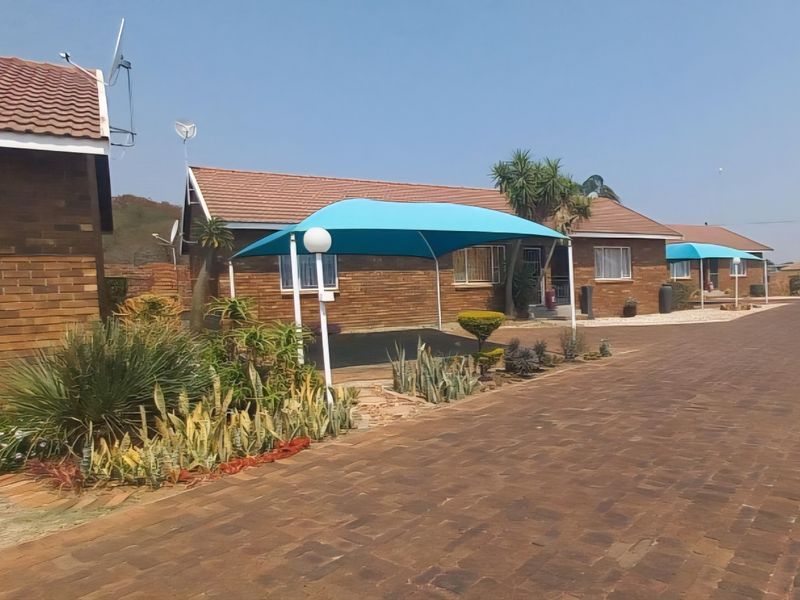 A view of the townhouse exterior featuring a face brick facade, tiled roof, and a paved driveway with a shade sail carport.