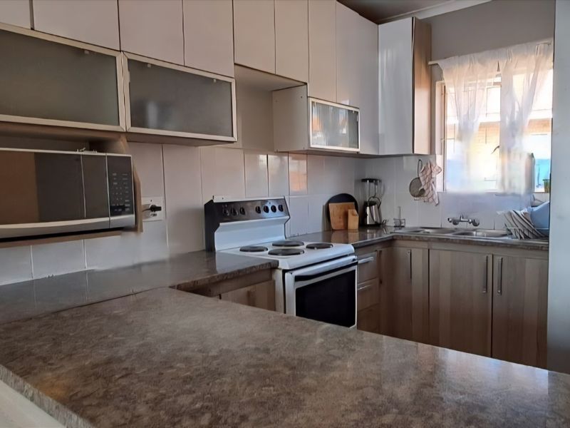 Functional kitchen featuring wood-look cabinetry, laminate countertops, tiled backsplash, and integrated electric stove with built-in microwave space.