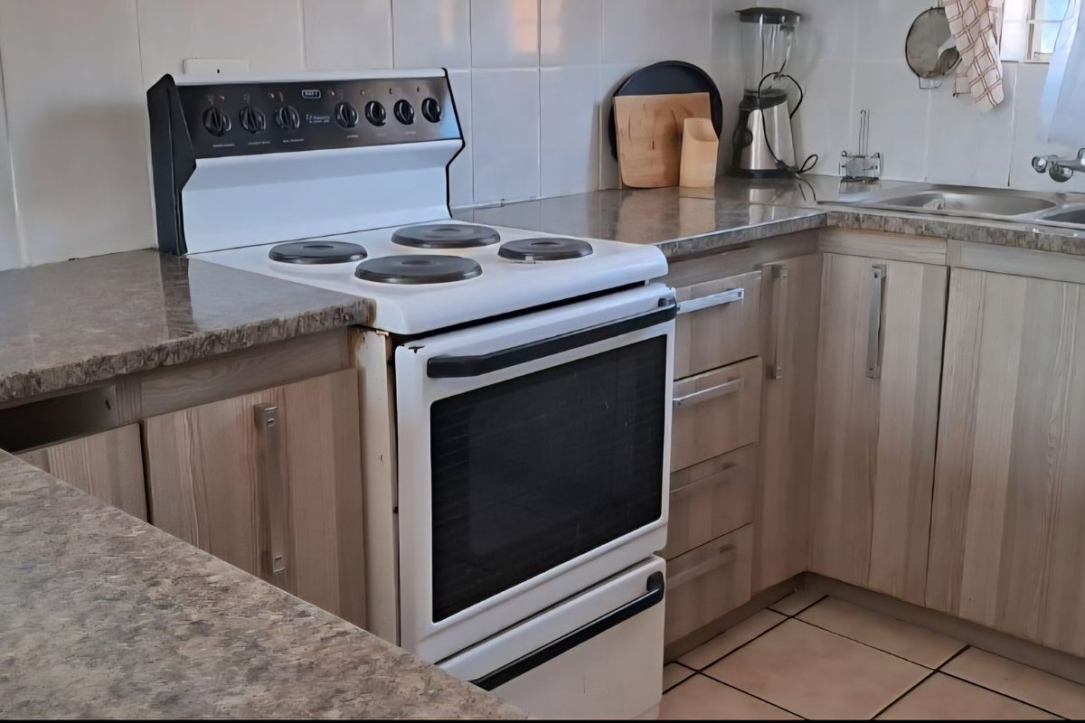 A functional kitchen featuring laminate cabinetry, stone-look countertops, a double bowl sink, and a freestanding electric stove with tiled splashbacks.