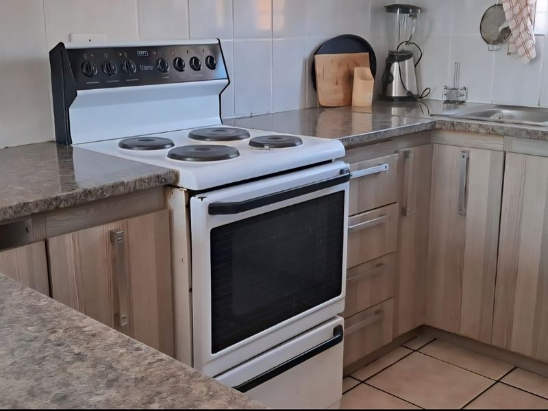 A functional kitchen featuring laminate cabinetry, stone-look countertops, a double bowl sink, and a freestanding electric stove with tiled splashbacks.