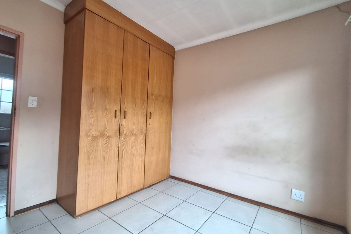A bedroom featuring built-in wooden cupboards, tiled flooring, and neutral wall finishes.