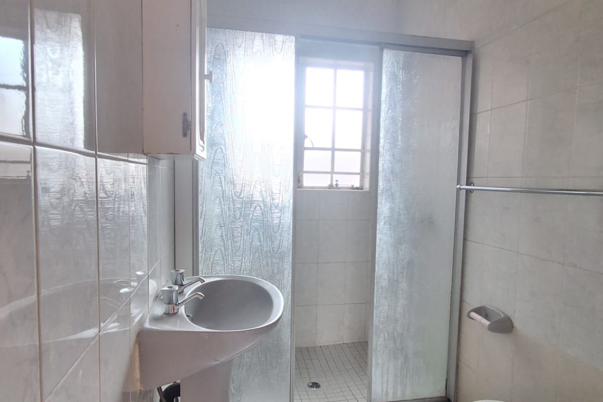 A functional bathroom featuring a pedestal basin, a shower with sliding glass doors, and tiled walls and flooring.