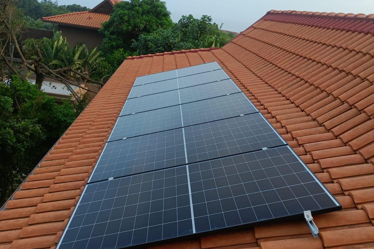 A high-angle view of a residential roof featuring installed solar panels on terracotta roof tiles.