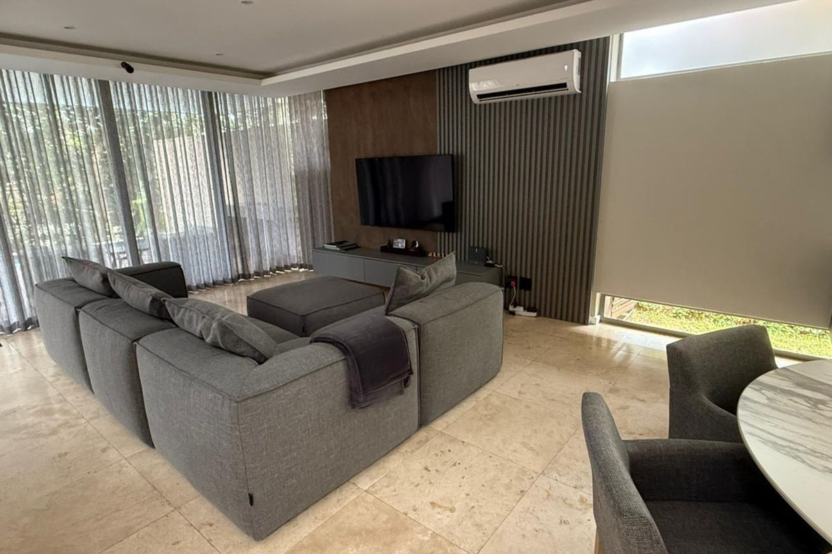 Modern living room featuring travertine flooring, a stylish slatted timber feature wall, recessed lighting, and floor-to-ceiling curtains with integrated air conditioning.