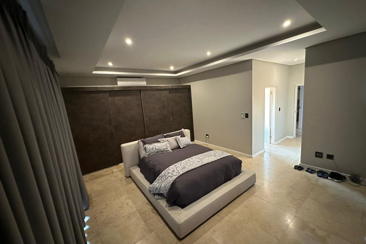 Spacious bedroom featuring modern recessed ceiling lighting, cove lighting, built-in cupboards, and tiled flooring with an integrated air conditioning unit.