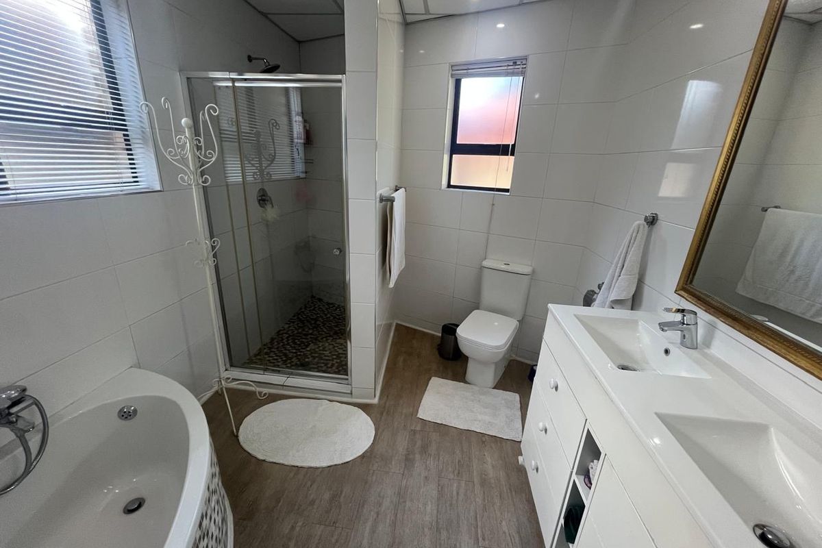 A well-appointed bathroom featuring a separate glass-enclosed shower, a corner bathtub, a double vanity with integrated sinks, and a toilet.