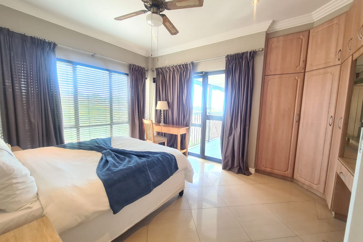 Spacious bedroom featuring built-in wooden cabinetry, tiled flooring, a ceiling fan, and direct access to a private balcony through glass sliding doors.