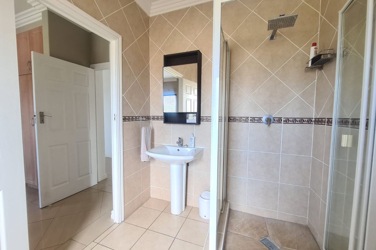 A functional bathroom featuring a pedestal basin, a glass-enclosed shower with a rainfall showerhead, and neutral wall and floor tiling.