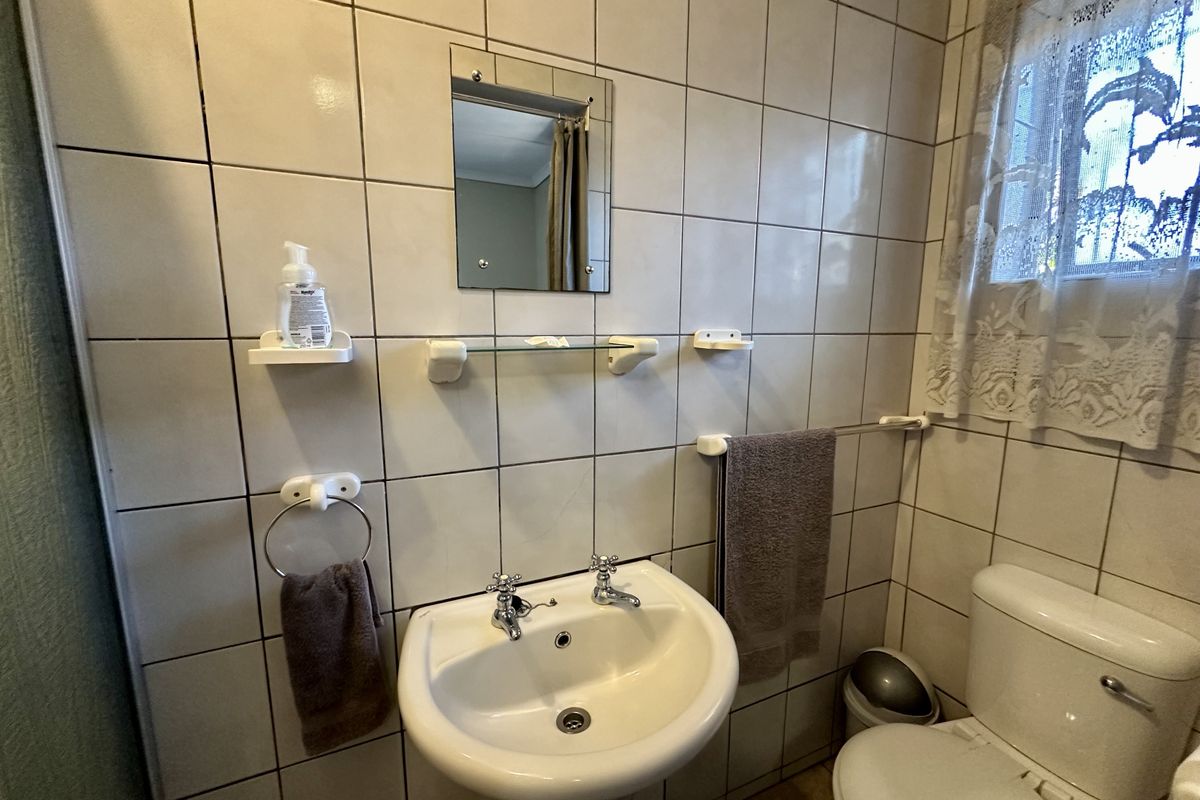 A functional bathroom featuring a pedestal basin, wall-mounted mirror, and standard toilet, finished with full-height wall tiling.