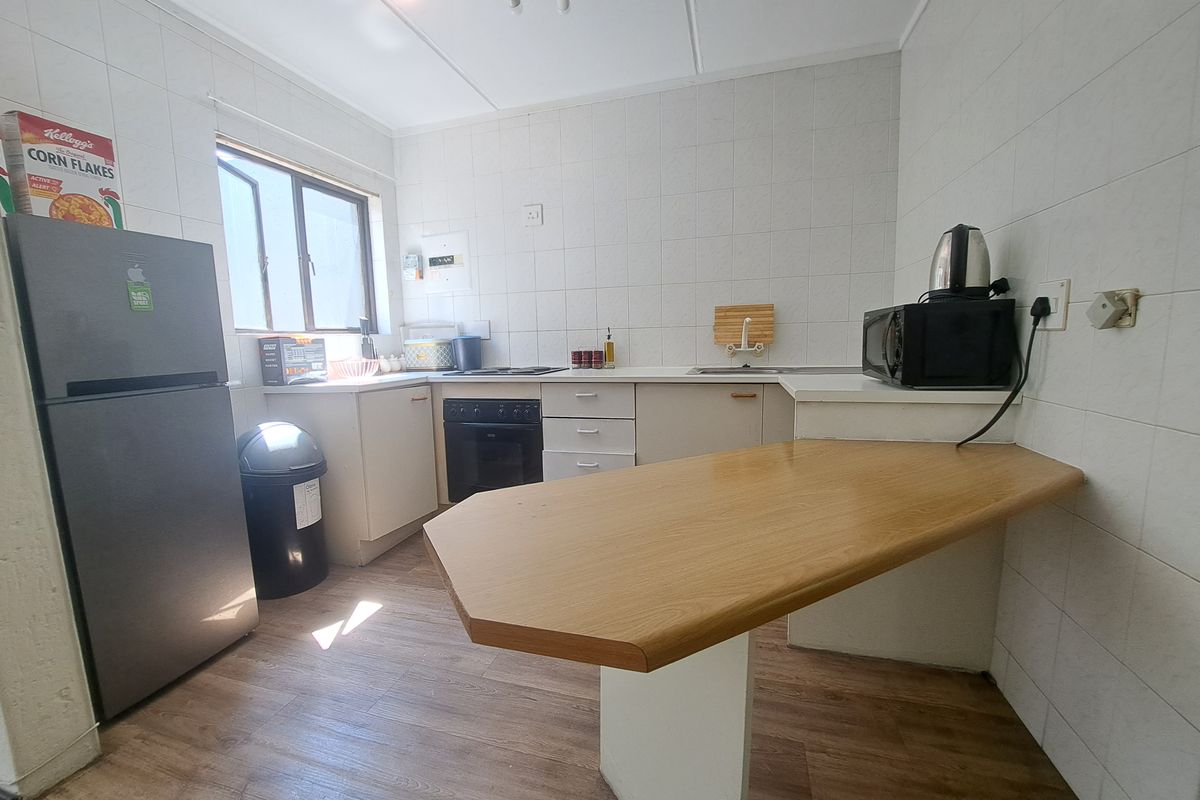 A functional kitchen featuring built-in cabinetry, a breakfast bar, electric hob, and oven, with tiled splashbacks and wood-look flooring.