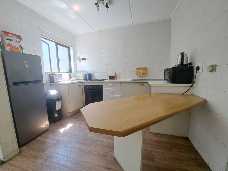 A functional kitchen featuring built-in cabinetry, a breakfast bar, electric hob, and oven, with tiled splashbacks and wood-look flooring.