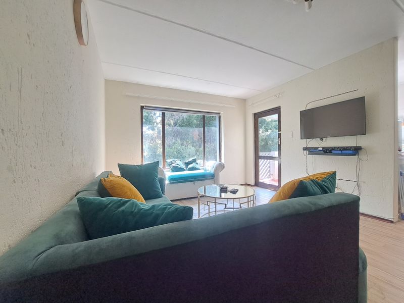A living room featuring laminate flooring, textured walls, and a large window providing natural light with access to an outdoor area.