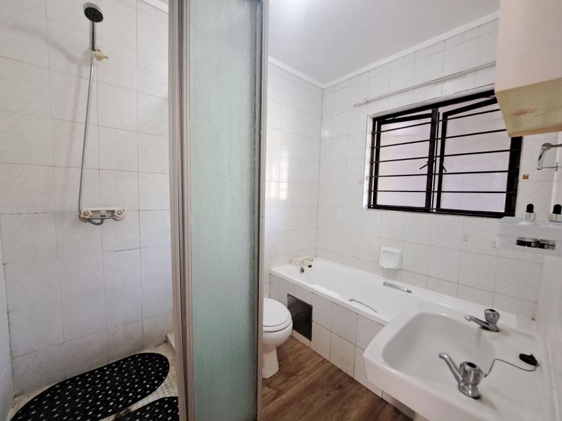 A functional bathroom featuring a separate shower, bathtub, pedestal basin, and tiled finishes, offering a clean space ready for potential modern updates.