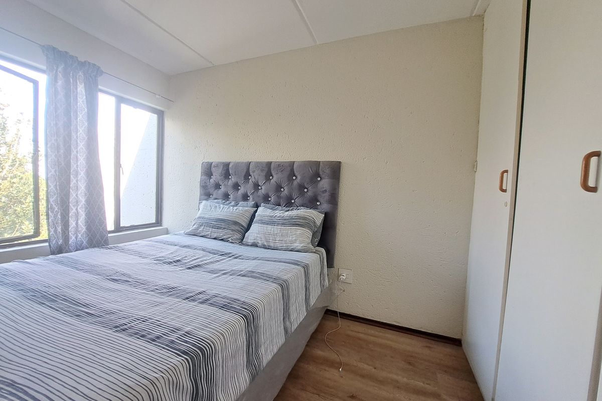 A functional bedroom featuring laminate flooring, built-in wardrobe storage, and natural light through aluminium-framed windows.