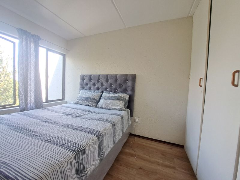 A functional bedroom featuring laminate flooring, built-in wardrobe storage, and natural light through aluminium-framed windows.