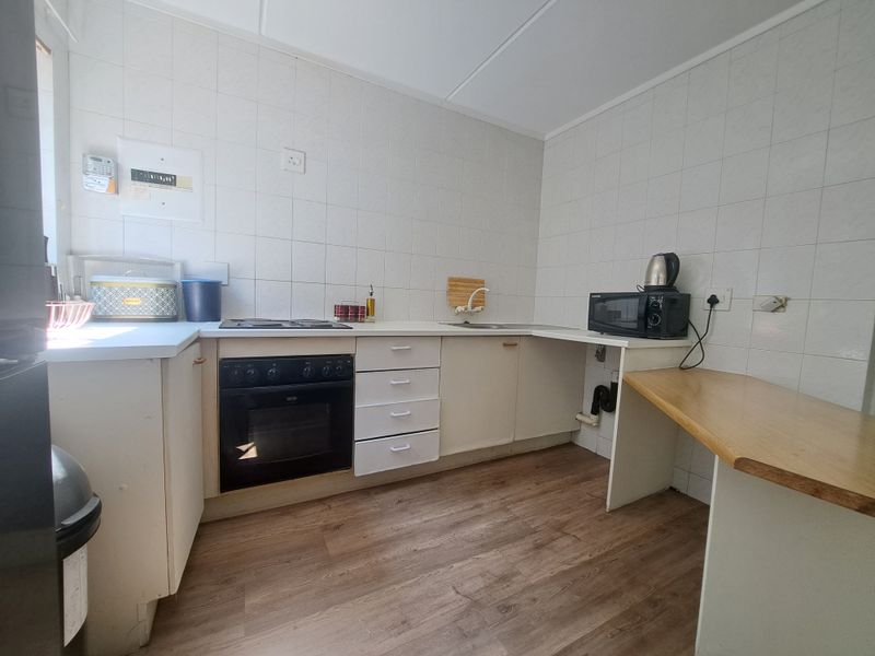 A functional kitchen featuring built-in cabinetry, an integrated oven and hob, tiled splashbacks, and wood-look laminate flooring.