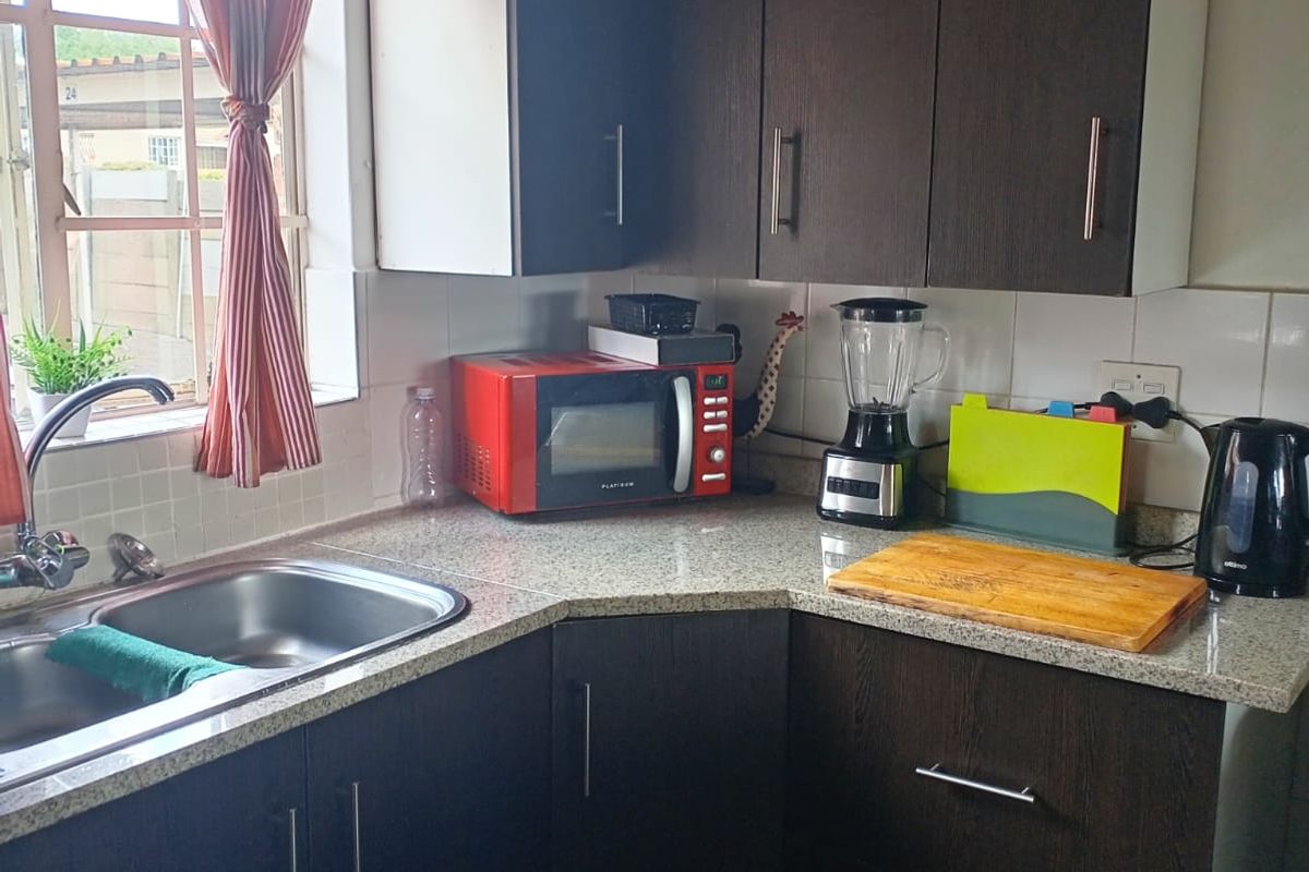 A functional kitchen corner featuring dark wood-finish cabinetry, granite-look laminate countertops, and a stainless steel double sink with a window view.