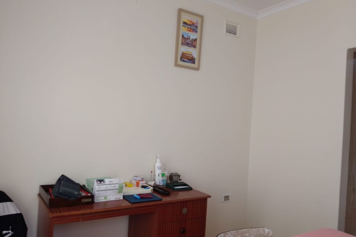A simple bedroom interior featuring plain walls, a ceiling vent, and a doorway leading to another area of the home.