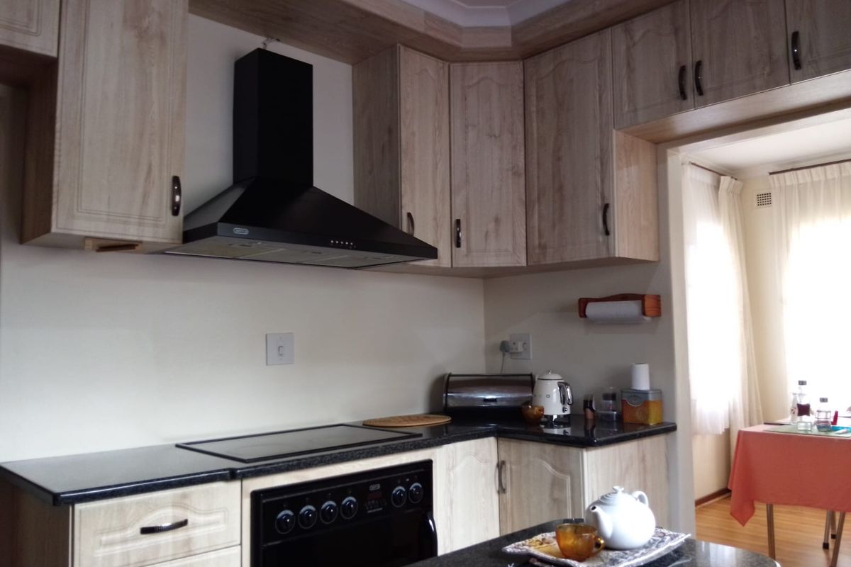 A functional kitchen featuring light wood-grain cabinetry, dark granite countertops, and a built-in black extractor fan and oven.