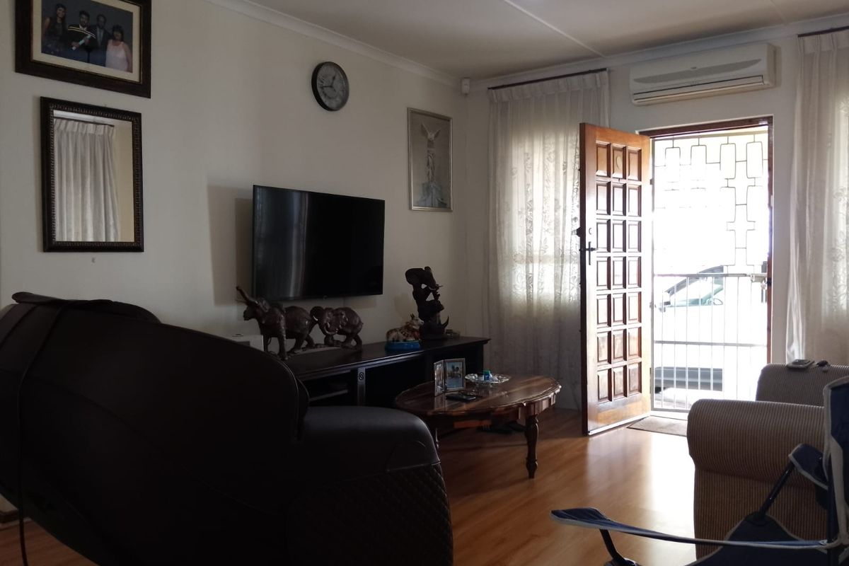 A living room featuring laminate flooring, a wall-mounted air conditioning unit, and a wooden entrance door with security gate.