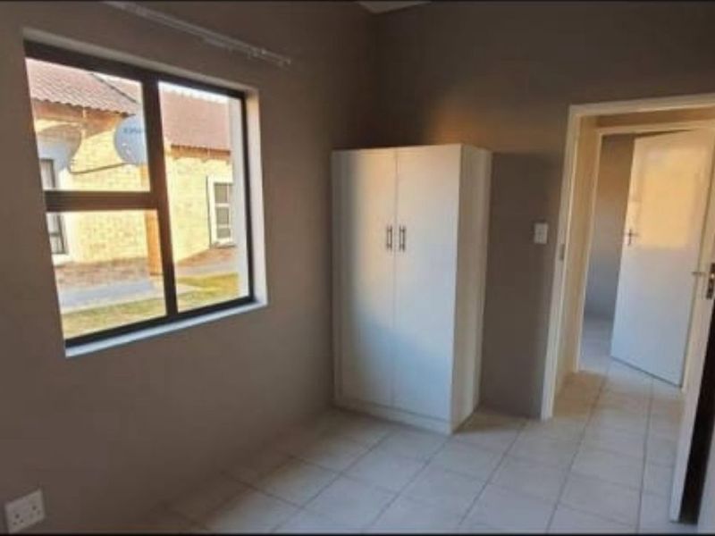 A simple, vacant bedroom featuring neutral wall tones, tiled flooring, and an aluminium-framed window, offering a clean canvas for personalization.