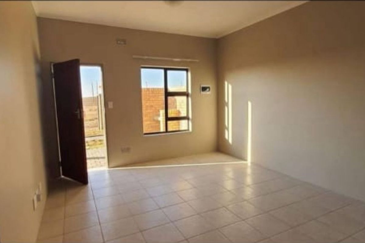An empty, neutral-toned living room featuring tiled flooring, an aluminium window, and direct access to the exterior.