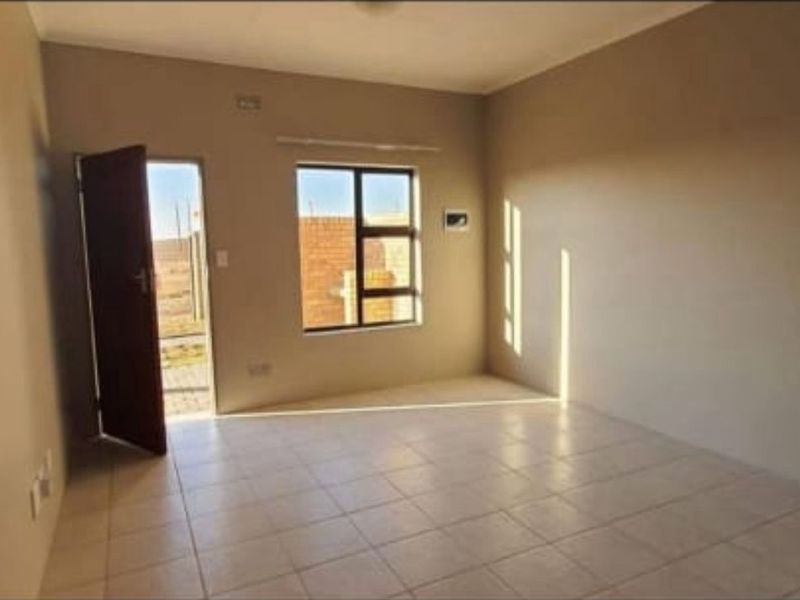 An empty, neutral-toned living room featuring tiled flooring, an aluminium window, and direct access to the exterior.