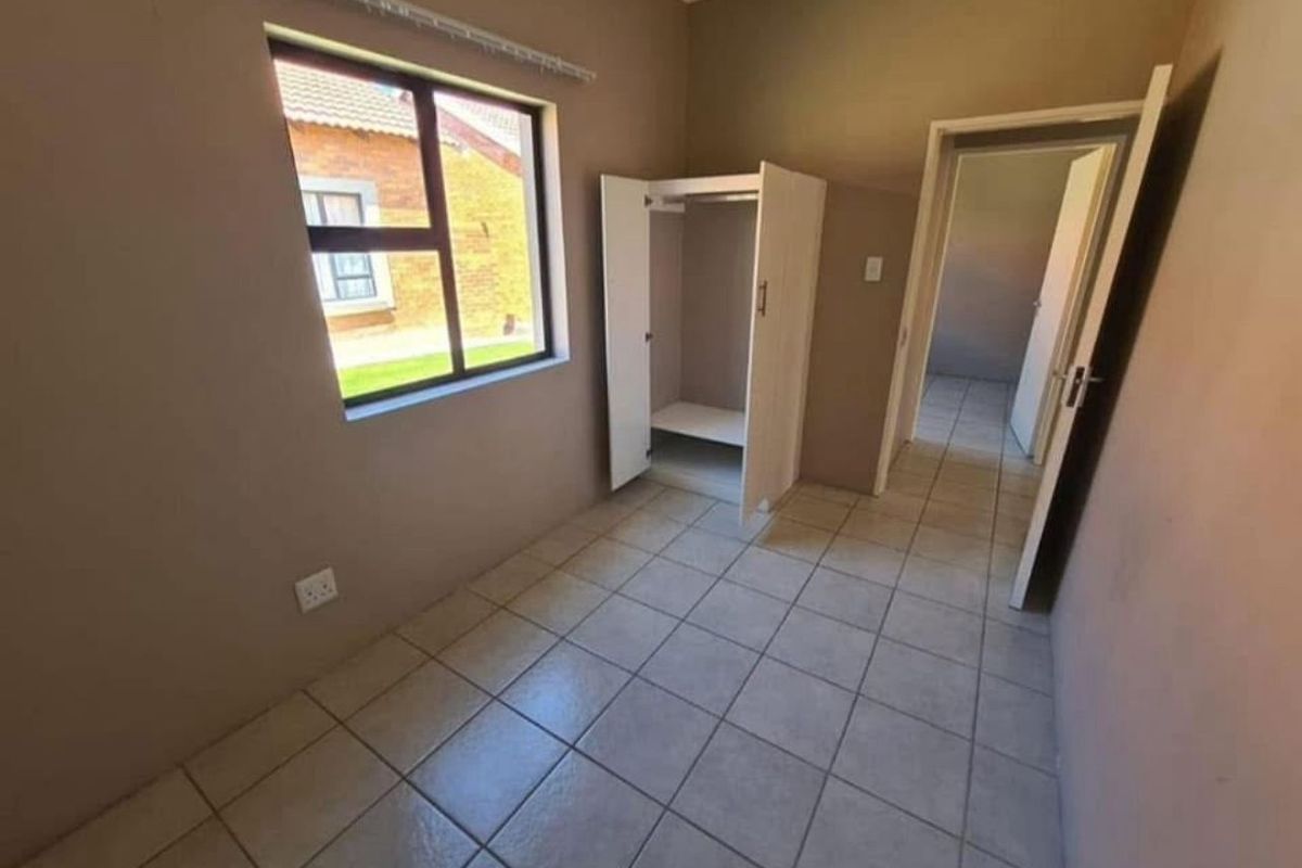 A vacant bedroom featuring tiled flooring, an aluminium window, and a built-in cupboard, offering a clean canvas for personalization.