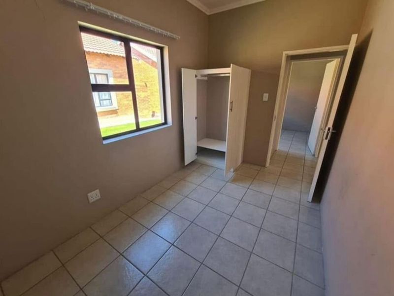 A vacant bedroom featuring tiled flooring, an aluminium window, and a built-in cupboard, offering a clean canvas for personalization.