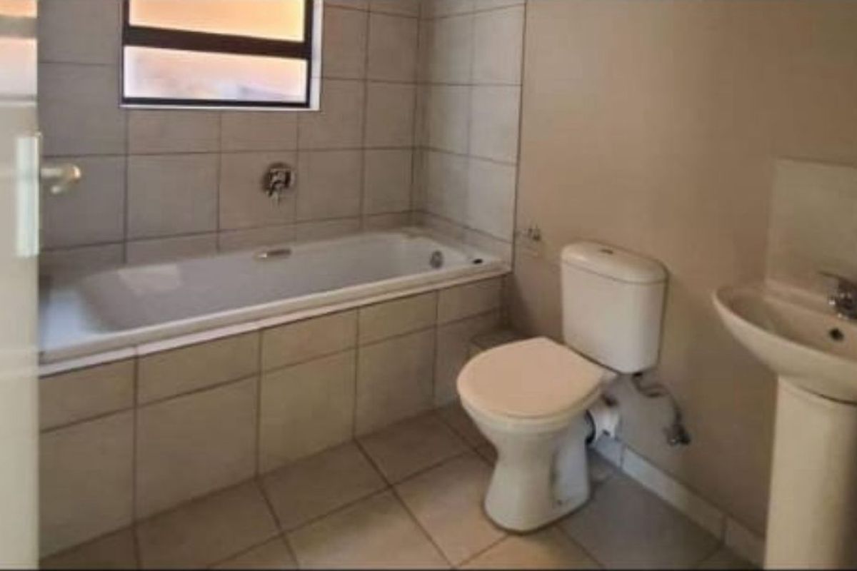 A functional bathroom featuring a bathtub, pedestal basin, and toilet with neutral tiled finishes throughout.