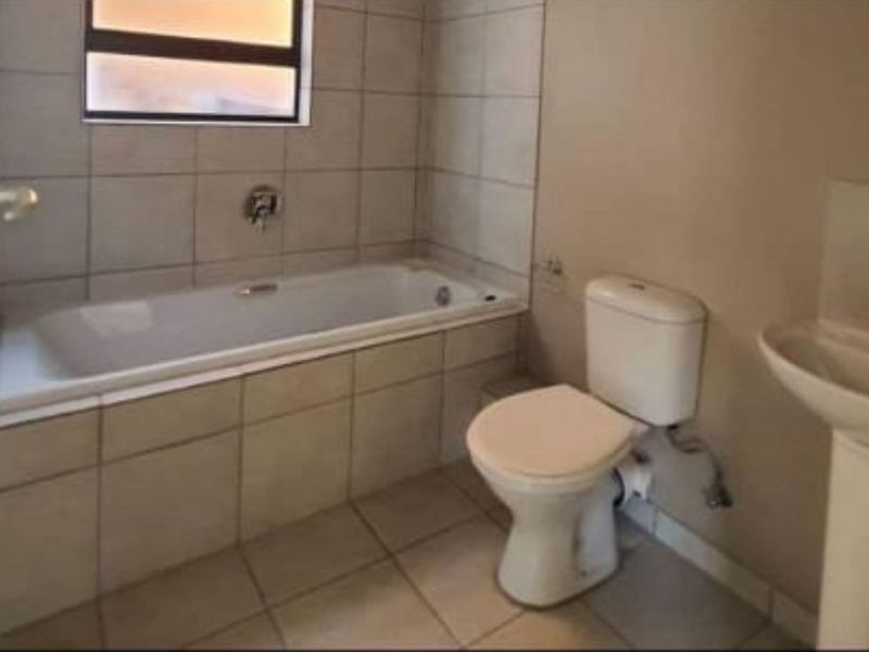 A functional bathroom featuring a bathtub, pedestal basin, and toilet with neutral tiled finishes throughout.