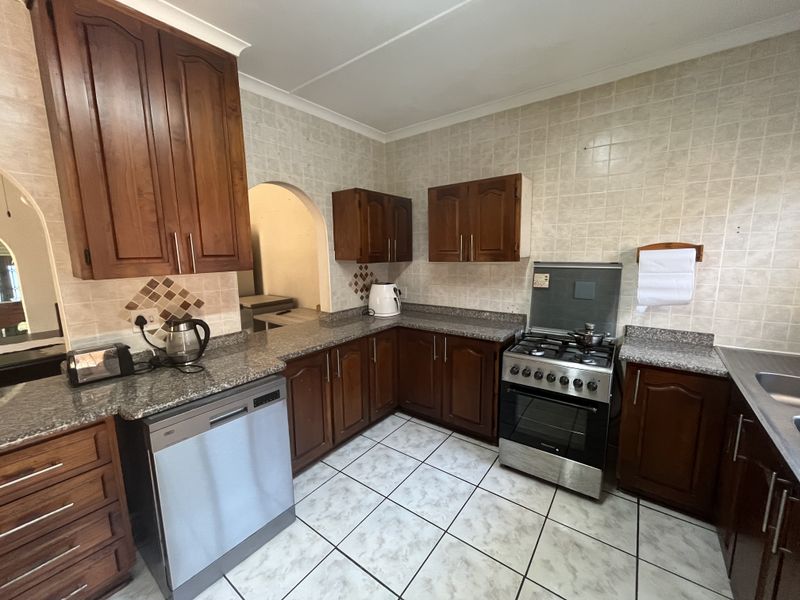 A functional kitchen featuring dark wood cabinetry, granite countertops, a gas stove, and tiled finishes throughout.