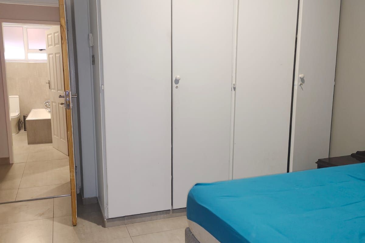 Bedroom featuring built-in floor-to-ceiling wardrobes and tiled flooring, with an adjoining en-suite bathroom visible through the doorway.
