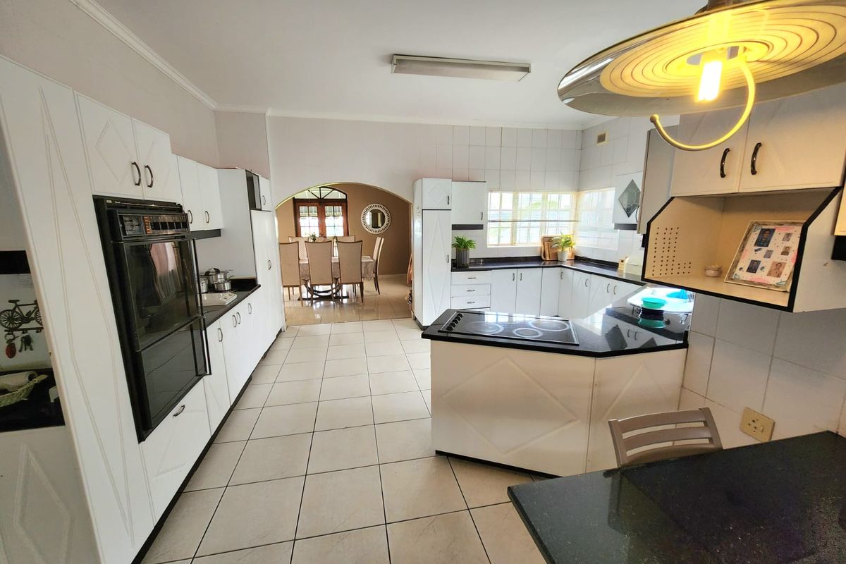 Spacious kitchen featuring white cabinetry, black granite countertops, built-in oven, and electric hob, with an open-plan flow leading into the dining area.