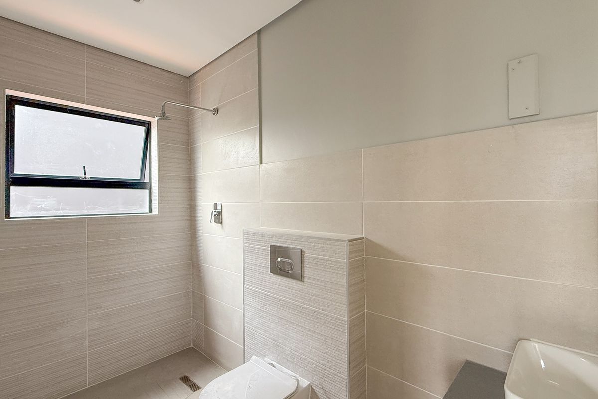 Modern bathroom featuring neutral wall tiles, a wall-mounted toilet with a concealed cistern, a walk-in shower area, and a sleek basin.