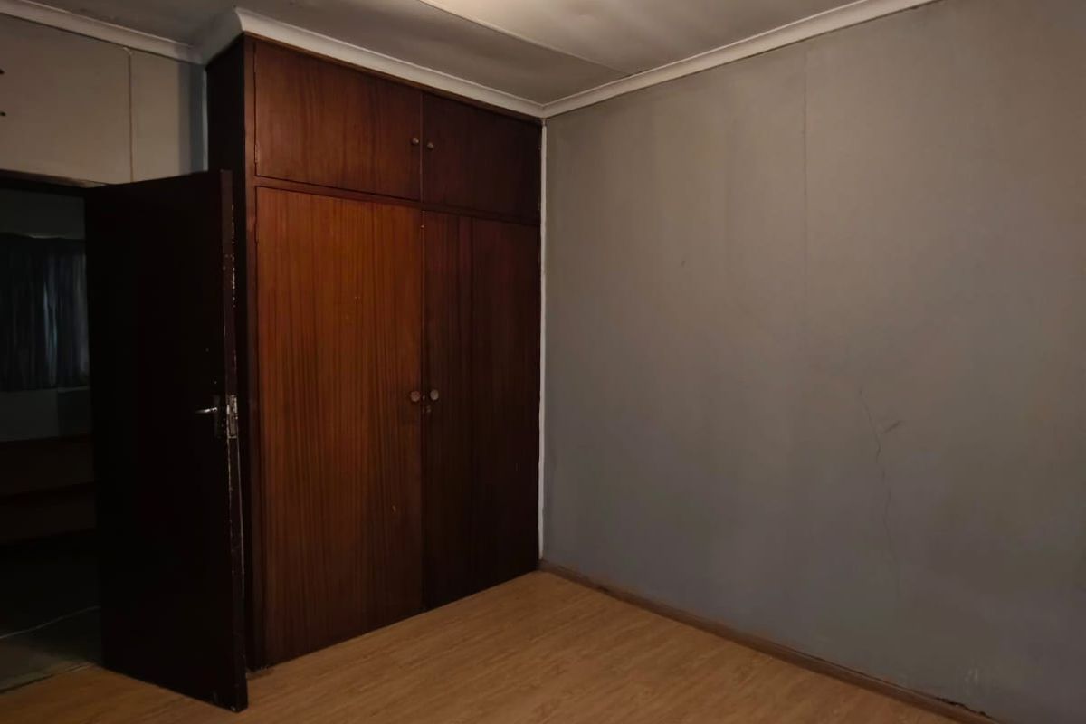 A vacant bedroom featuring built-in wooden cupboards, laminate flooring, and a central ceiling light fixture.