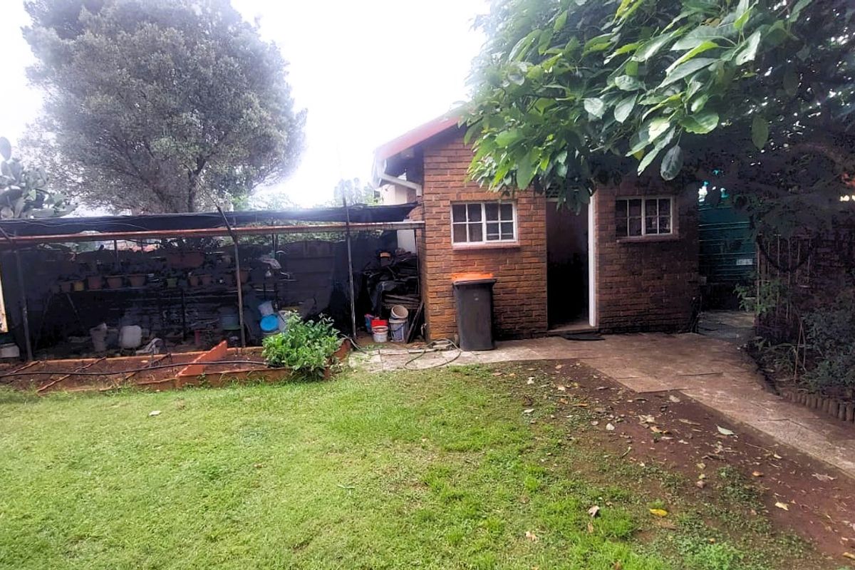 Rear garden area featuring a brick outbuilding, a covered storage structure, and a lawn with paved pathways.
