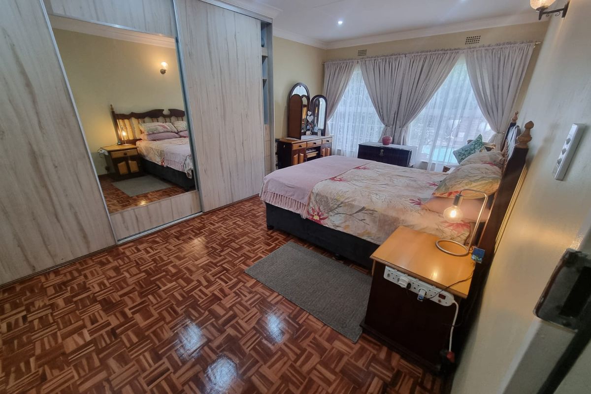 A well-maintained bedroom featuring polished parquet flooring, built-in sliding door wardrobes with mirrored panels, and recessed ceiling lighting.