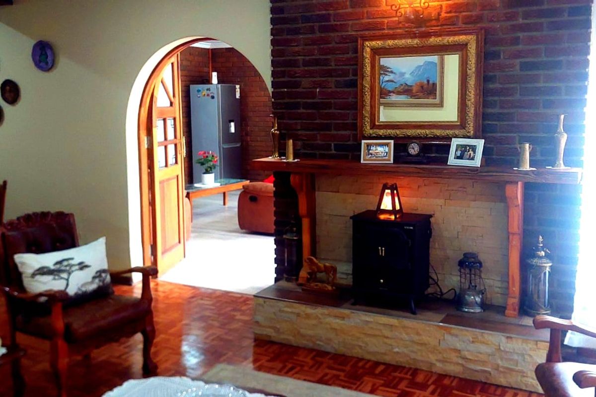 A cozy living room featuring a prominent brick fireplace with a wooden mantel, parquet flooring, and an arched doorway leading to an adjacent room.