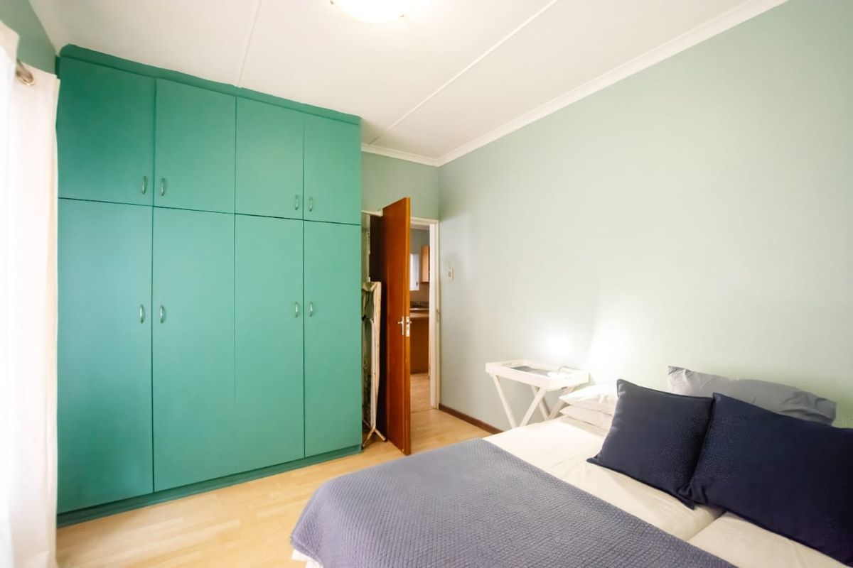 A bedroom featuring light green walls, laminate flooring, and floor-to-ceiling built-in cupboards providing ample storage space.