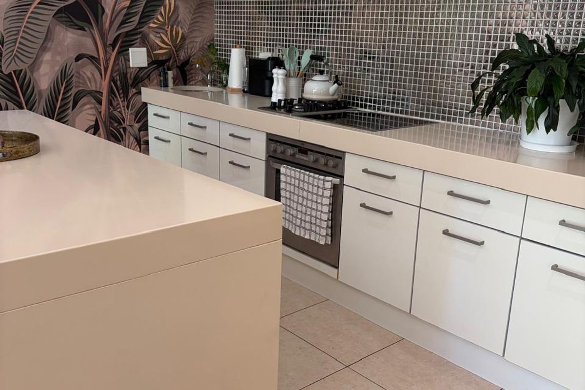 Modern kitchen featuring sleek white cabinetry, a stone-topped island, mosaic tile backsplash, built-in oven, and a stainless steel extractor fan.