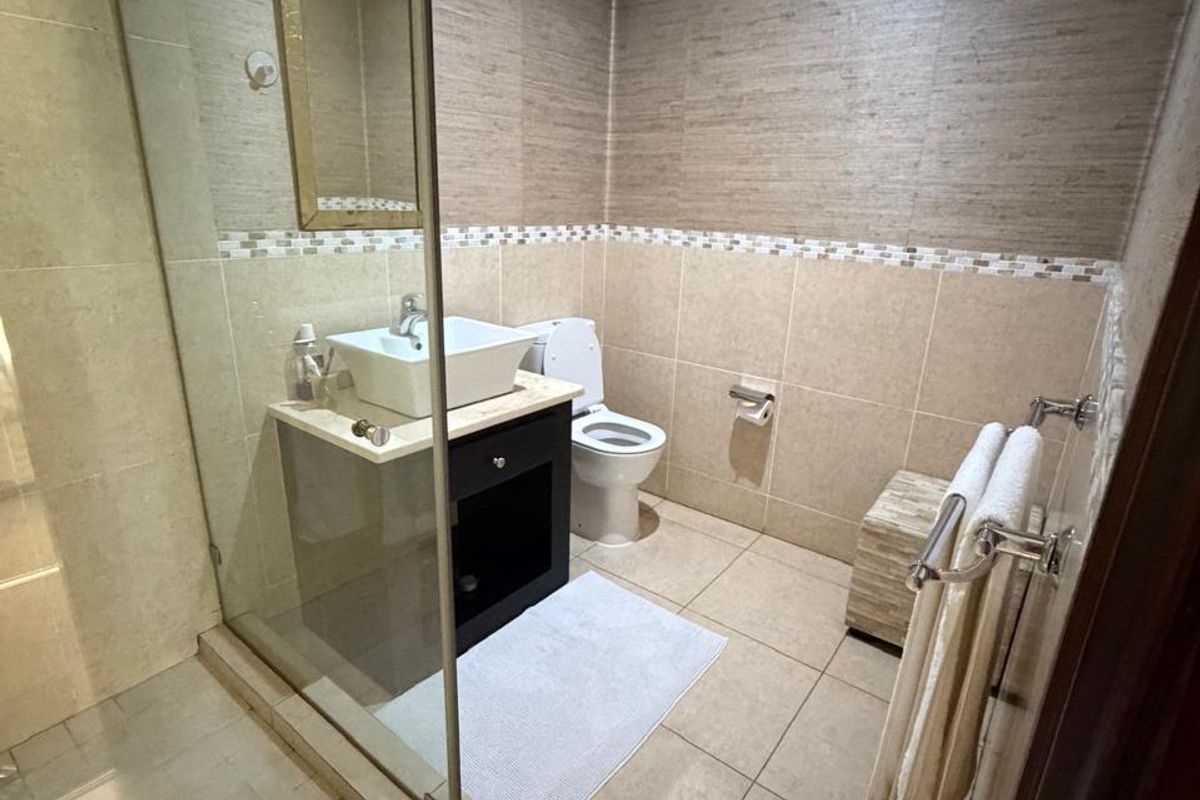 A modern bathroom featuring a glass-enclosed shower, a vessel sink vanity, and neutral-toned wall and floor tiling.
