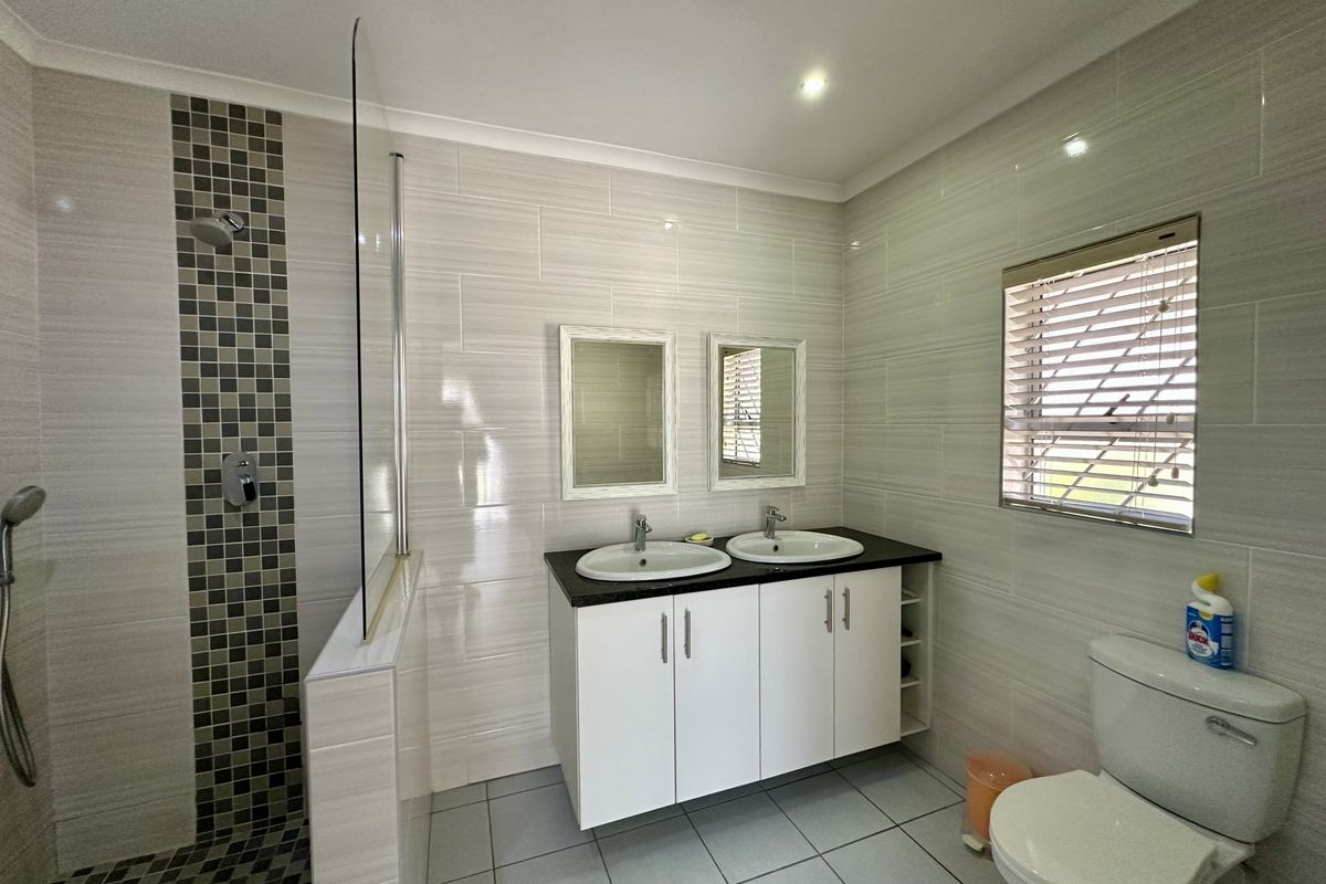 Modern bathroom featuring a double vanity with integrated sinks, a walk-in shower with glass partition, and neutral wall tiling.