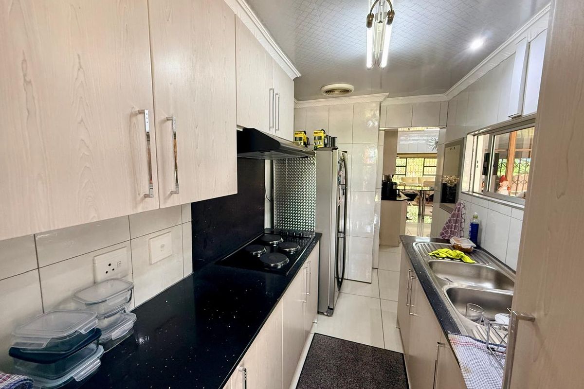 A functional galley-style kitchen featuring light wood-grain cabinetry, black stone countertops, a built-in hob with extractor fan, and a double stainless steel sink.
