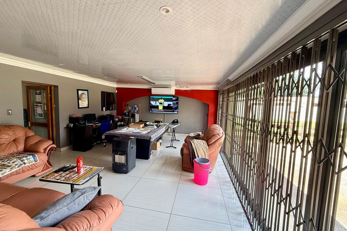 Spacious living area featuring large format floor tiles, recessed ceiling lighting, wall-mounted air conditioning unit, and secure metal sliding security gates.