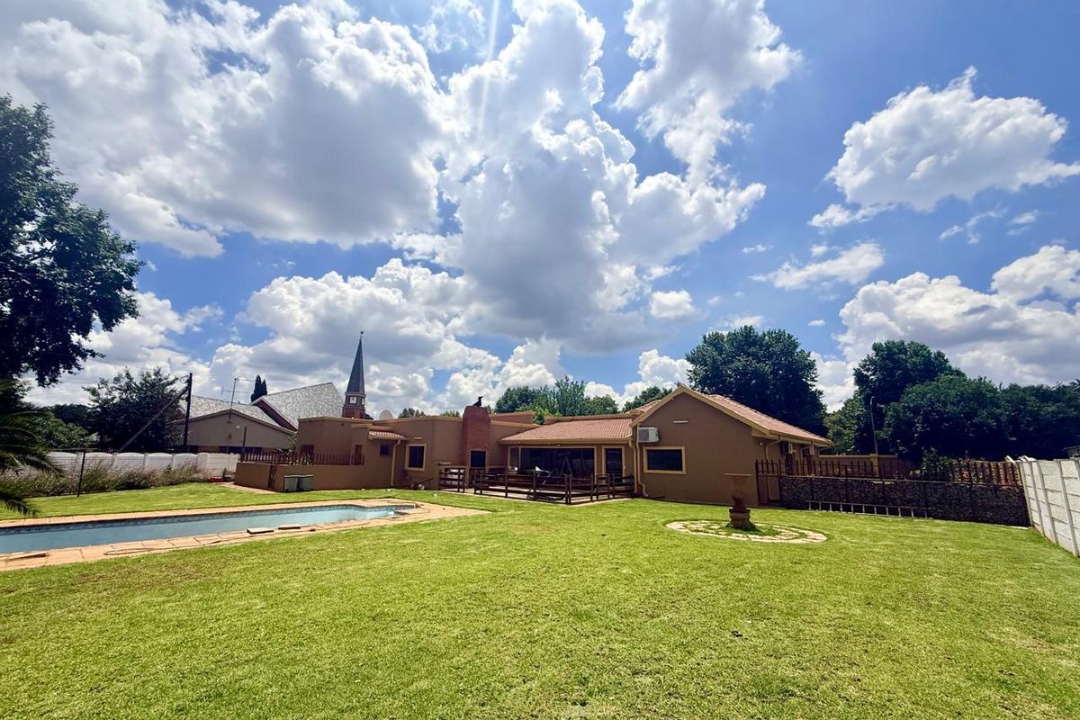 Spacious rear garden featuring a swimming pool, expansive lawn, and a covered patio area attached to the main house structure.
